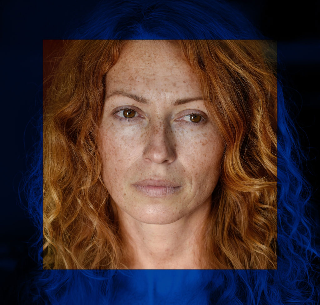 Immagine che raffigura una donna quarantenne in primo piano con i capelli rossi e le lentiggini con lo sguardo pensieroso